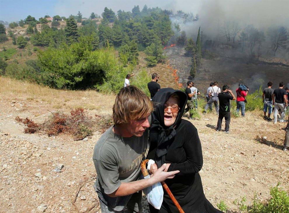 Пожилую женщину эвакуируют по мере приближения лесного пожара  к деревне Варнава. (Orestis Panagiotou/EPA)