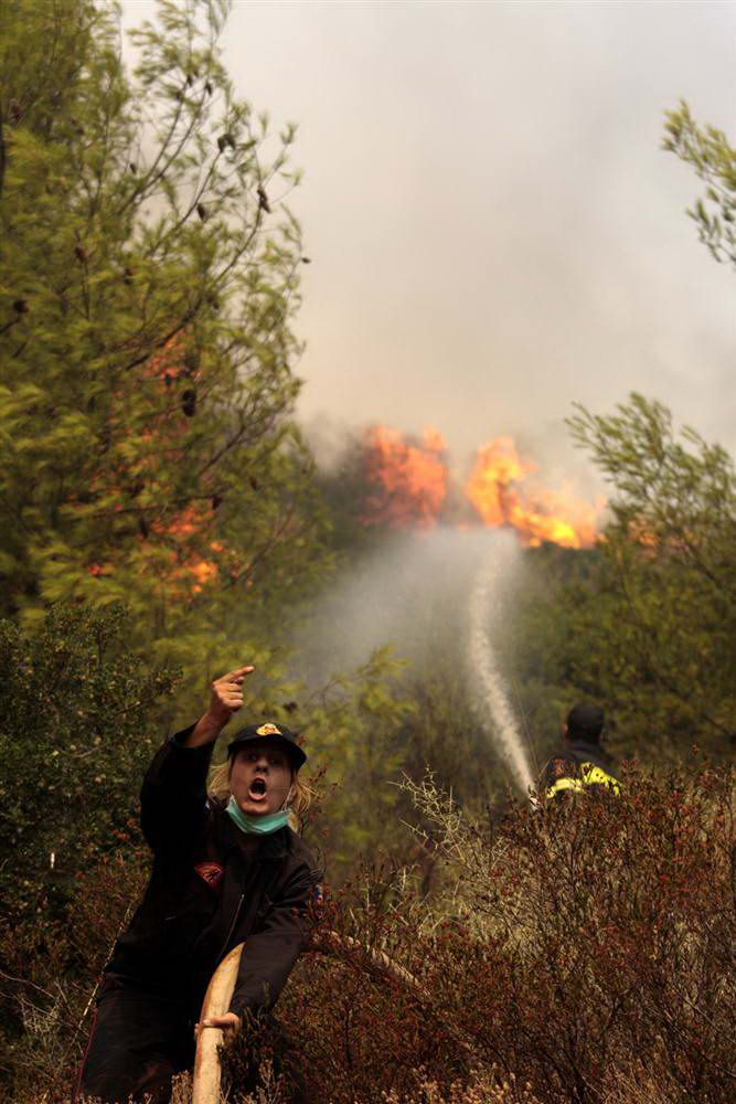 Женщина-пожарный кричит коллеге, чтобы тот открыл насос, во время сдерживания пожара у деревни Марафон. (Dimitri Messinis/AP)