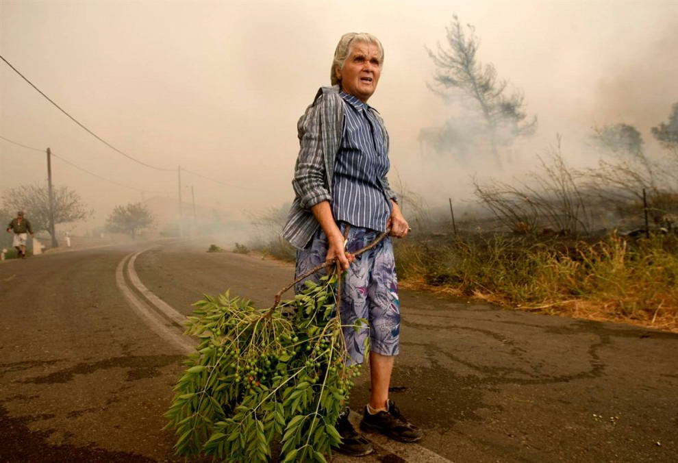 Пожилая женщина держит ветку, стоя посреди улицы во время лесного пожара у деревни Грамматико к северо-востоку от Афин. (Yiorgos Karahalis/Reuters)