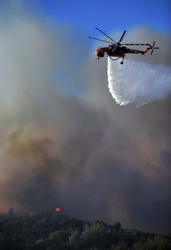 Пожарный вертолет сбрасывает воду на горящий лес в Агиос Стефанос в воскресенье.  (Nikolas Giakoumidis/AP)