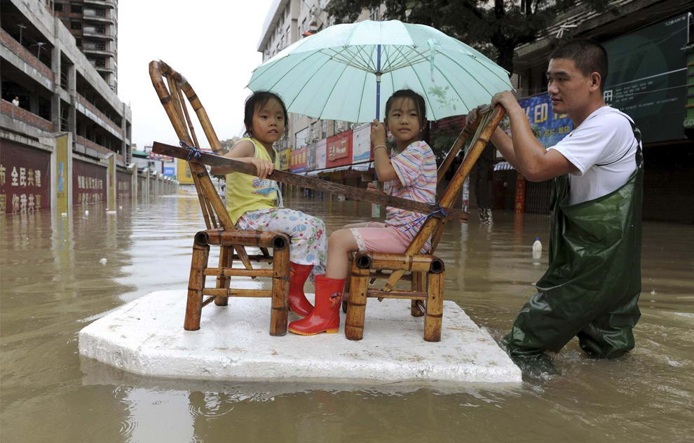 Житель толкает самодельный плот, чтобы перевезти на другую сторону затопленной улицы двух девочек после того, как тайфун Моракот прошел по округу Цаньнань в китайской провинции Чжэцзян 10 августа 2009 года. (REUTERS/Lang Lang)