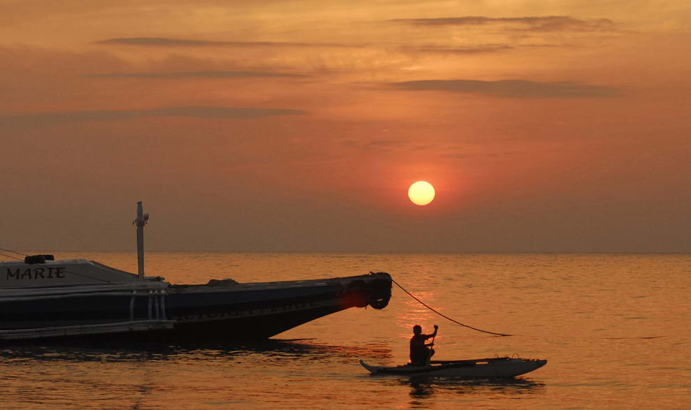 Рыбак проплывает на своем каноэ мимо рыбацкого судна. Фото сделано на центральном филиппинском острове Себу на восходе 9 августа 2009 года, после окончания продолжительного дождя, который принес сюда тайфун Моракот. (REUTERS/Victor Kintanar)