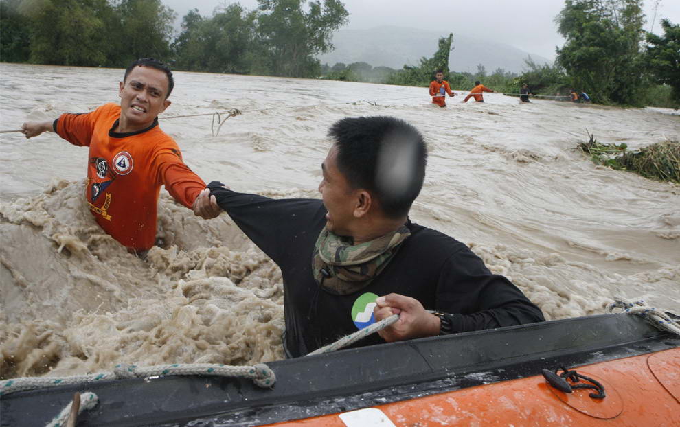 Филиппинский спасатель помогает коллеге во время пересечения затопленного района с сильным течением в городе Ботолан, северные Филиппины 7 августа 2009 года. Город Ботолан погрузился в воду в пятницу, после того как в городе прорвало плотину. (REUTERS/Erik de Castro)