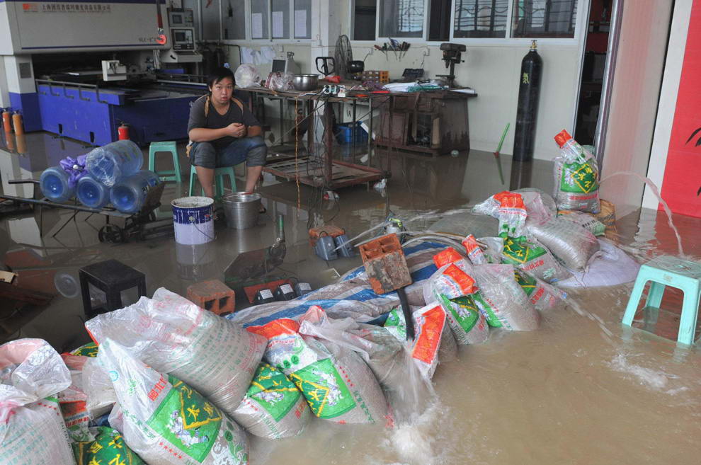 Рабочий сидит за грудой мешков с песком, пока насосы выкачивают воду из его мастерской. Это – последствия того, что тайфун Моракот достиг Фучжоу, провинция Фуцзянь 9 августа 2009. (REUTERS/Kong Nong)