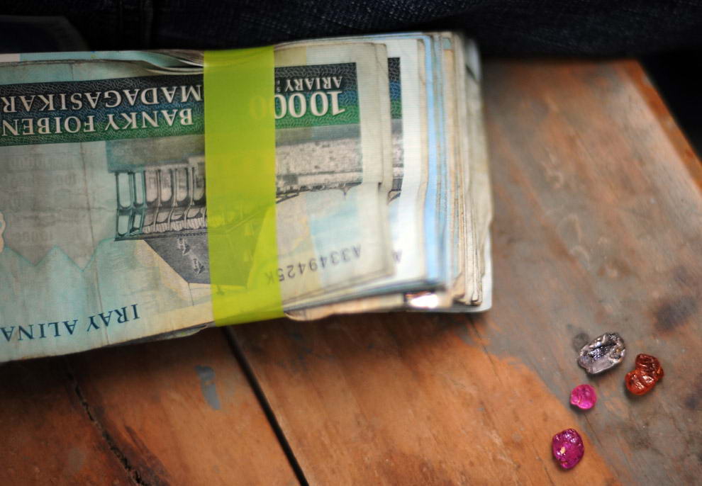 Четыре сапфира рядом с пачкой банкнот в ювелирной мастерской, где покупатель драгоценных камней со Шри-Ланки оценивает сапфиры,