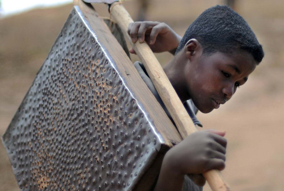10-ти летний Франсуа Рантонирина несет лопату и самодельное сито, с помощью которых они с матерью в поисках сапфиров все утро просеивали гравий