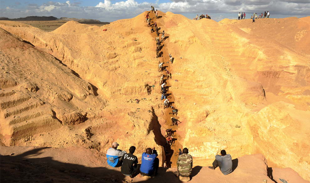 Пятеро мужчин наблюдают за группой старателей, которые достают гравий и песок из большой сапфировой шахты