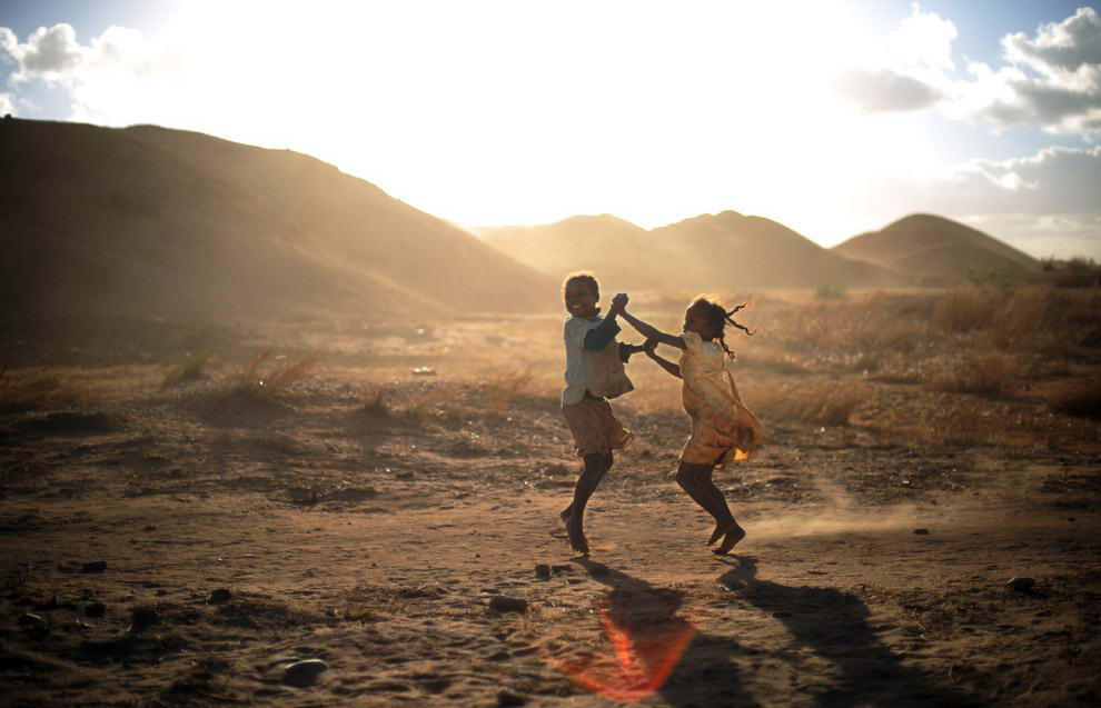 Мандраисара (справа) и ее подруга Тафитасоаниана (слева) возле гор песка и гравия танцуют и поют под песню, которую они услышали по местной популярной радиостанции. 