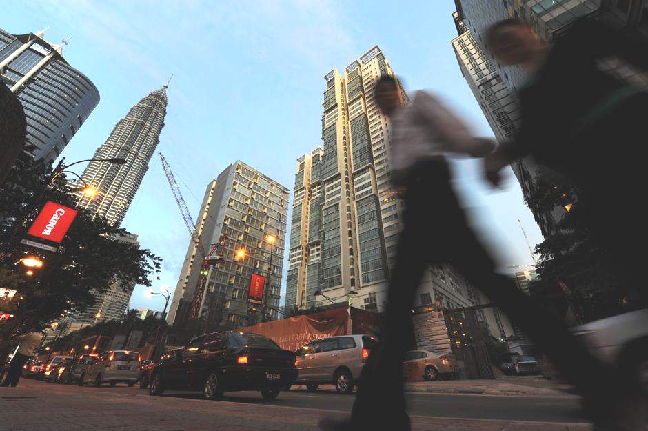 Офисные работники проходят на фоне небоскребов в центре Куала-Лумпура.