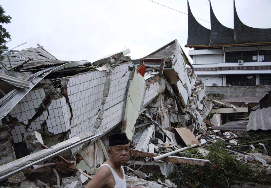 Человек стоит перед рухнувшим зданием после землетрясения в Паданге, на острове Суматра в Индонезии.