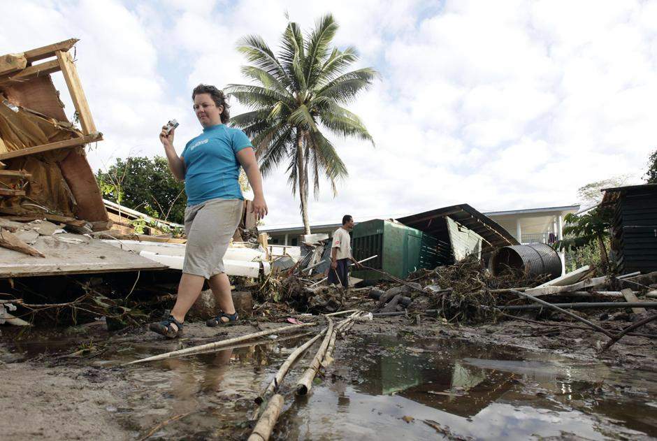 Гражданка США Хитер Пеннер, сотрудница «Coconut Resort» в Maninoa Siumu на южном побережье проходит мимо разрушенного цунами курортный комплекс, в котором она работала.