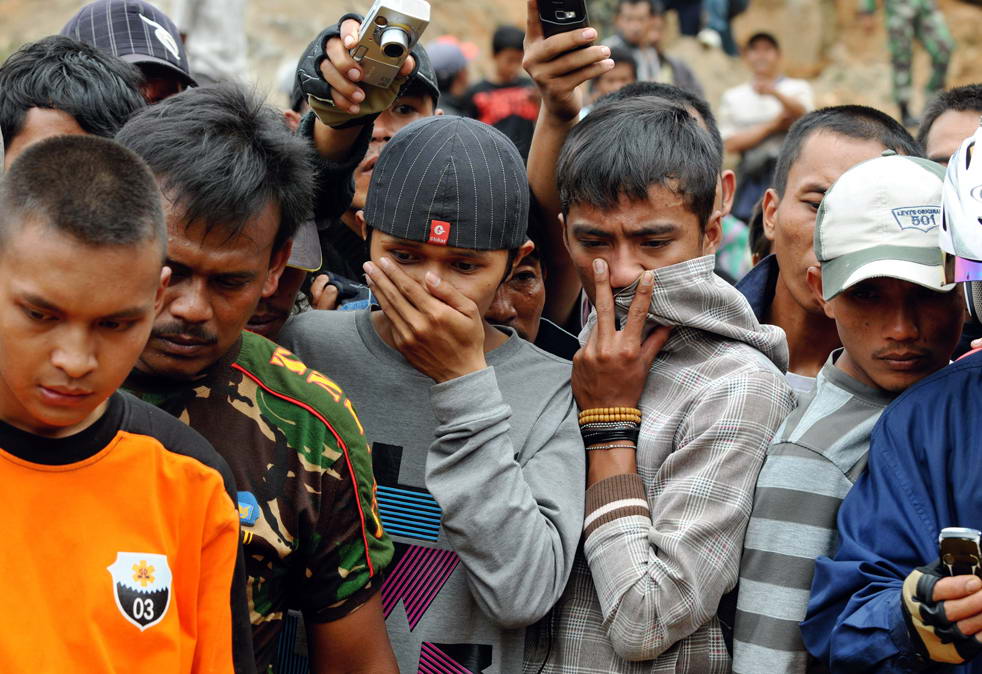 Жители смотрят на то, как индонезийские солдаты, полиция и местные жители поднимают тело жертвы оползня. Снимок сделан в деревне Pamoyanan в Сибинонге 3 сентября. (AFP/Getty Images/Adek Berry)